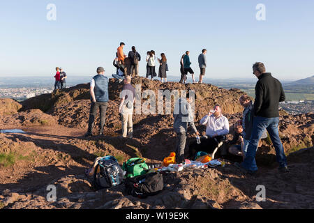Les visiteurs et un groupe d'hommes avec des boissons et des aliments de l'été profiter du soleil du soir sur le sommet du siège d'Arthur à Holyrood Park, surplombant la ville d'Édimbourg, le 26 juin 2019, à Édimbourg, en Écosse. Arthur's Seat est un volcan éteint qui est considéré comme le pic principal du groupe de collines à Édimbourg, en Écosse, qui constituent l'essentiel de Holyrood Park, décrite par Robert Louis Stevenson comme 'une colline pour l'ampleur, d'une montagne en vertu de son design audacieux'. La colline s'élève au-dessus de la ville d'une hauteur de 250,5 m (822 ft), offrant une excellente vue panoramique de la ville et au-delà. Banque D'Images