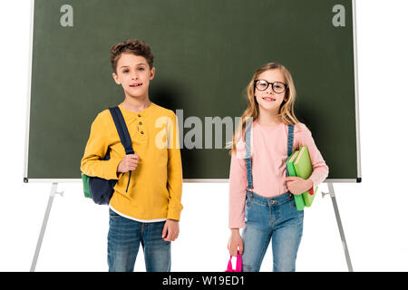 Deux écoliers avec sacs à dos et les livres debout près de blackboard isolated on white Banque D'Images