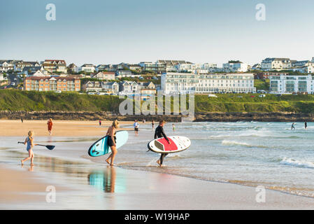 Les vacanciers transportant paddle boards dans la mer à la plage de Fistral à Newquay en Cornouailles. Banque D'Images