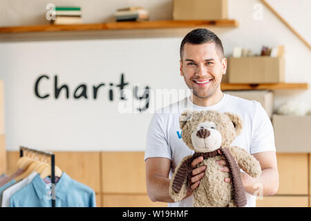 Beau, joyeux volunteer holding teddy bear and looking at camera Banque D'Images