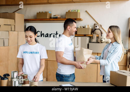 Les jeunes bénévoles multiculturels en donnant de la nourriture à la jolie femme au centre de bienfaisance Banque D'Images