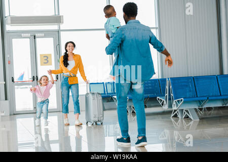African American woman avec fille marcher vers mari avec fils in airport Banque D'Images