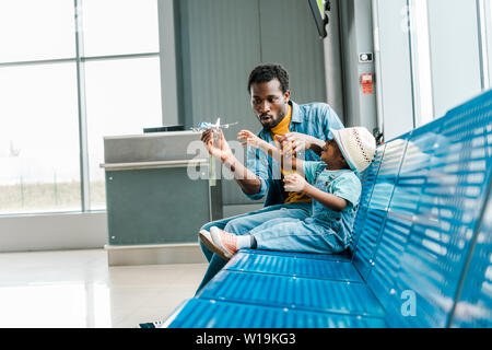 African American father avec grimace et son fils assis dans la salle d'attente dans les aéroports et l'Playing with toy plane Banque D'Images