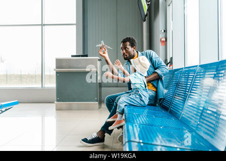 L'accent african american father and son sitting in hall d'attente dans les aéroports et l'Playing with toy plane Banque D'Images