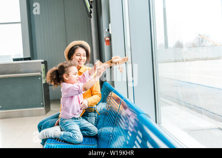 Happy african american mother and daughter sitting in airport et jouer avec un modèle d'avion Banque D'Images