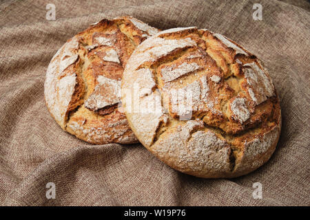 Le pain brun fond Lin rustique Vue du haut vers le bas. Deux grain de seigle entier cuit au four à pain fait maison Circle sur le sac textile. Boulangerie artisanale nourriture Frais Roun Banque D'Images