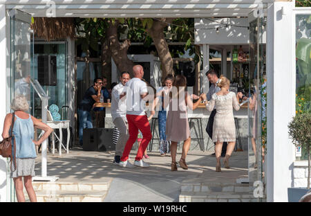 La Canée, Crète, Grèce. Juin 2019. Les clients danser autour du bar d'un restaurant grec dans la région de Crète Chania. vu par un passant. Banque D'Images