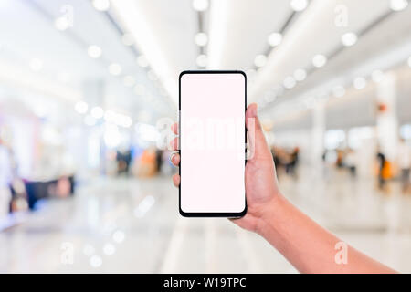 Image de la maquette hand holding mobile phone avec écran blanc avec blur office corridor couloir bokeh background light,écran blanc maquette modèle caractéristique Banque D'Images
