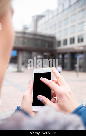 Businesswoman utilise un téléphone mobile dans la rue contre un immeuble de bureaux. Banque D'Images