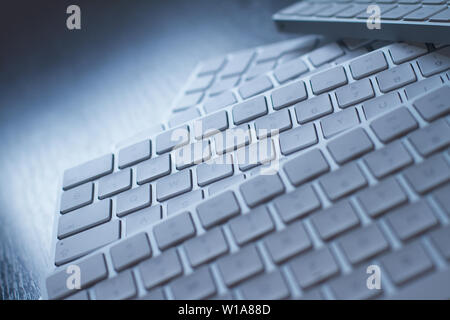 Gros plan vue perspective d'un grand nombre de claviers d'ordinateur en aluminium blanc sans fil sur l'autre sur un bureau en bois noir avec lumière naturelle Banque D'Images