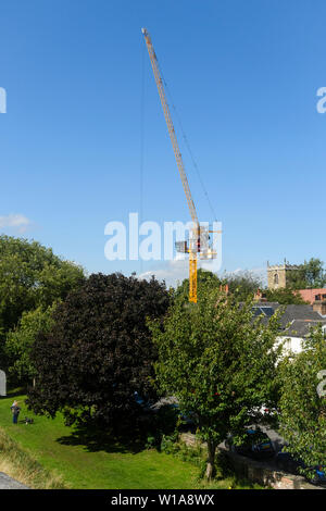 Tall Yellow Crane Tower & levage working on construction site contre ciel bleu profond (cabine, mât & jib) - York, North Yorkshire, Angleterre, Royaume-Uni Banque D'Images