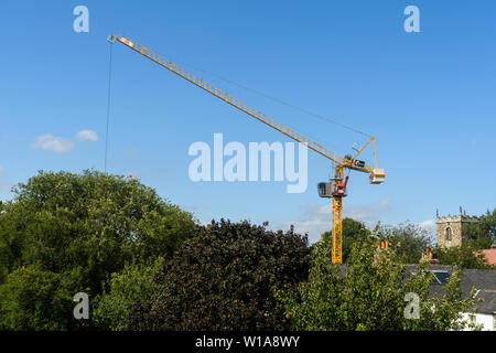 Tall Yellow Crane Tower & levage working on construction site contre ciel bleu profond (cabine, mât & jib) - York, North Yorkshire, Angleterre, Royaume-Uni Banque D'Images