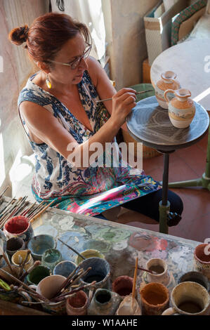 Artisane peint deux petits pots en céramique dans son magasin. Différents types de pinceaux et couleurs sur son banc. Banque D'Images