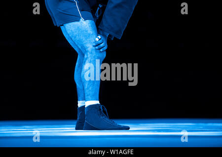 La lutte des hommes sur un tapis de lutte jaune dans la salle de sport. Filtre de couleur bleu.