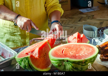 Close up of a woman slicing up une pastèque avec un couteau de cuisine sur un plan de travail. Banque D'Images