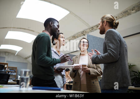 Low angle view au groupe ethnique multi -affaires de gens rire joyeusement tout en discutant pendant pause café dans office, copy space Banque D'Images