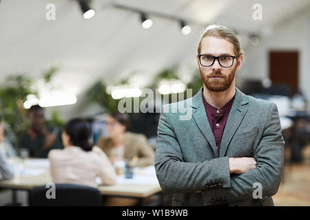 Jusqu'à la taille de l'homme portrait barbu portant des lunettes posing in office with and looking at camera, copy space Banque D'Images