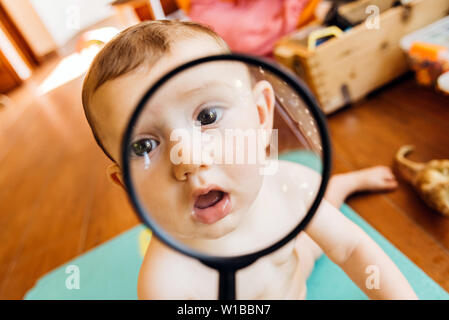 Baby face en jouant avec une loupe, ce qui en fait un drôle et tendre visage. Banque D'Images