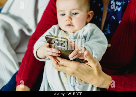 Bébé sur le bras de sa mère en train de jouer avec un téléphone mobile pour explorer le monde virtuel. Banque D'Images