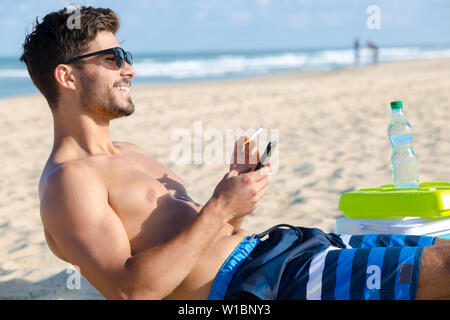 Jeune homme de fumer et en utilisant son téléphone sur la plage Banque D'Images