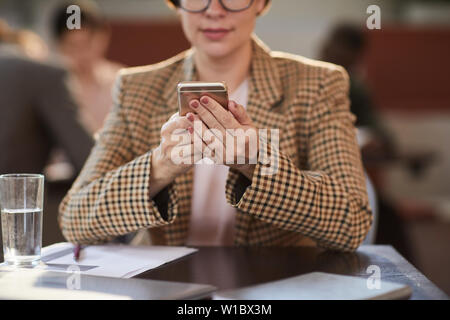 Cropped portrait of businesswoman holding smartphone contemporain tout en travaillant à table dans un café, copy space Banque D'Images