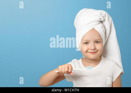 Portrait d'une petite fille sur un fond bleu. Un enfant avec une serviette blanche sur la tête tenant une brosse à dents. Le concept de l'hygiène quotidienne. Banque D'Images