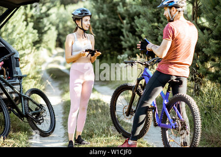 L'homme et la femme les cyclistes qui portent des gants et un casque, de se préparer pour l'équitation de vélo tout en se tenant sur la route forestière pendant l'été Banque D'Images