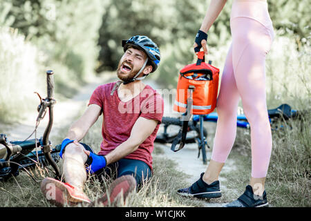 Femme de l'administration des premiers soins à un homme avec une blessure au genou en faisant du vélo sur la montagne des vélos sur la route forestière pendant l'été Banque D'Images