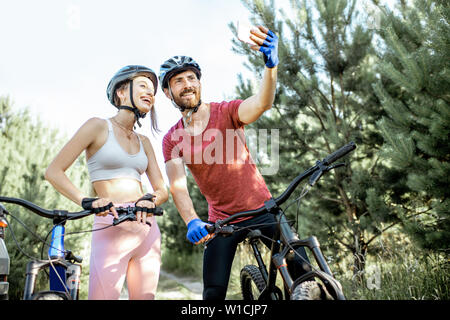 Sports jeunes couple taking photo selfies avec smartphone pendant l'équitation, des vélos de montagne sur la route forestière pendant l'été Banque D'Images