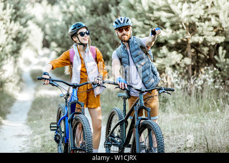 Jeune couple voyageant avec des vélos de montagne dans la forêt, montrant l'homme avec la main sur la voie à suivre Banque D'Images