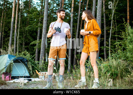 Young couple de boissons chaudes sur le camping dans la forêt, profitant de leur voyage d'été au coucher du soleil Banque D'Images