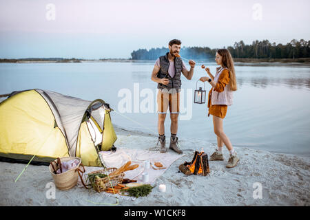 Young couple having fun at le camping sur la plage, debout près de la cheminée dans la soirée Banque D'Images