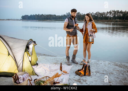 Young couple having fun at le camping sur la plage, debout près de la cheminée dans la soirée Banque D'Images