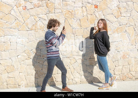 Jeune homme de prendre une photo de sa petite amie posant devant l'appareil photo de son smartphone Banque D'Images
