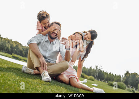 Devinez qui heureux jeune famille de quatre et s'amuser pendant que smilin sitting on grass in park. Pique-nique. Week-end Banque D'Images