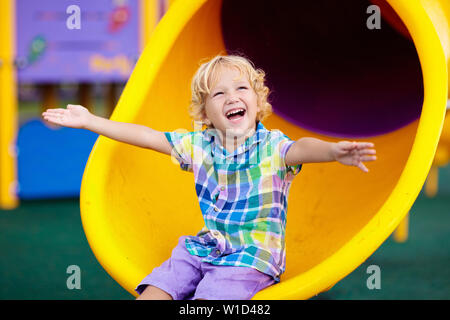 Enfant jouant sur l'aire de jeux extérieure. Les enfants jouent sur l'école ou l'école maternelle cour. Kid active sur diapositive colorées et swing. Activité d'été sain pour chi Banque D'Images