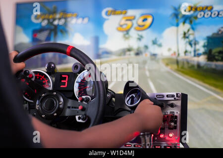 Un enfant jouant un jeu de course de style arcade et en utilisant le bouton de commande du simulateur de pilotage. Banque D'Images