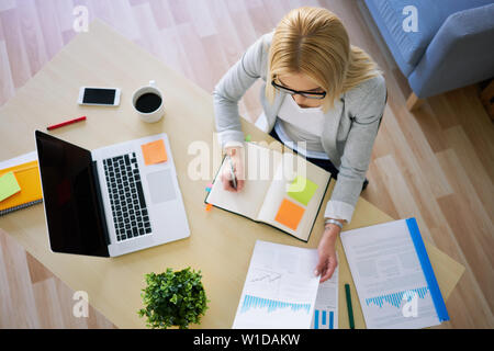 Vue de dessus de jeune femme travaillant avec ordinateur portable et notebook in home office Banque D'Images