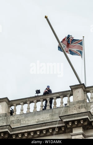 Londres, Royaume-Uni. Sur un toit élevé sous un drapeau britannique en lambeaux, un policier balaye une foule de manifestants à travers des jumelles à fort grossissement Banque D'Images