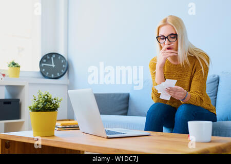 Inquiets young woman sitting on sofa at home à reçus et factures à Banque D'Images