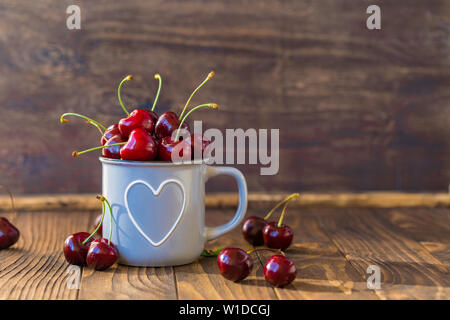 Cerises fraîches en gris tasse en forme de coeur sur table en bois, teinté Banque D'Images