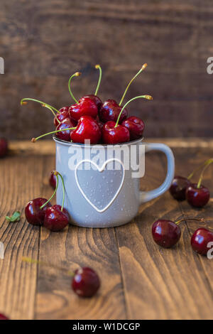 Cerises fraîches en gris tasse en forme de coeur sur table en bois, teinté Banque D'Images