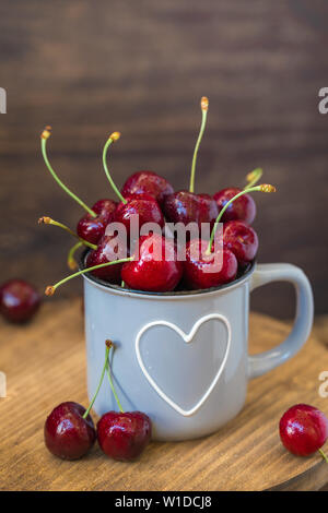 Cerises fraîches en gris tasse en forme de coeur sur table en bois, teinté Banque D'Images