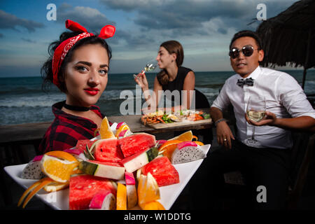 Amis dans un restaurant de fruits de mer - cheers clink verres et serveuse avec fruit dans l'avant-plan Banque D'Images