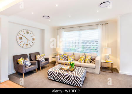 Salle de séjour avec un canapé élégant et un centre de table avec des tapis gris et l'horloge murale derrière le sofa. Banque D'Images