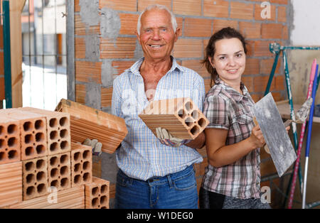 Jeune femme heureuse et confiante man avec outils et matériaux dans les mains dans leur chambre réparables Banque D'Images