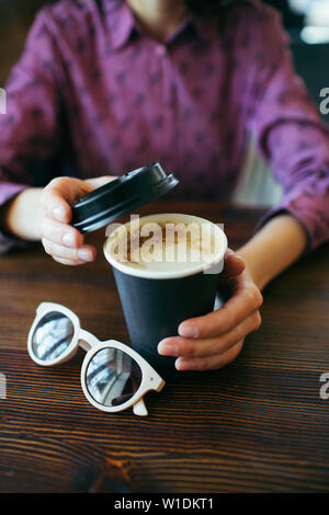 Les mains tenant une tasse de Cappuccino avec une mousse épaisse à emporter en noir en papier. Le café à emporter. Banque D'Images