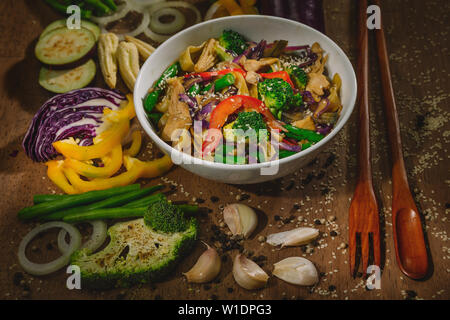 Wok faire sauter des légumes avec des courgettes, des champignons, des asperges de printemps, du paprika, des carottes et du brocoli avec du poulet et des nouilles, servis dans un bol blanc Banque D'Images