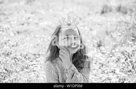 L'humour reine concept. Fille est assise sur l'herbe à grassplot, fond vert. Fille sur le visage rieur qui passent à l'extérieur loisirs. Enfant posant avec un sourire en carton les lèvres et couronne pour séance photos à Meadow. Banque D'Images