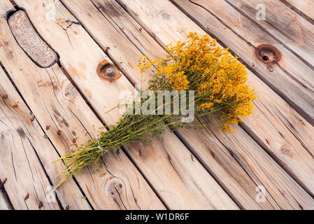 Un godet de séché du millepertuis (hypericum perforatum) avec des fleurs jaunes et verts tiges fixées sur un tambour de câble rustique ancienne venverted dans une table. Banque D'Images